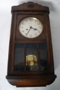 An oak cased wall clock with brass movement, enamel dial, pendulum and key.