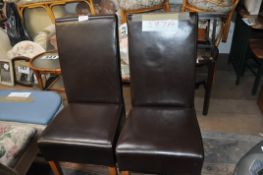 A pair of contemporary leather dining chairs standing on square legs with all over leather style
