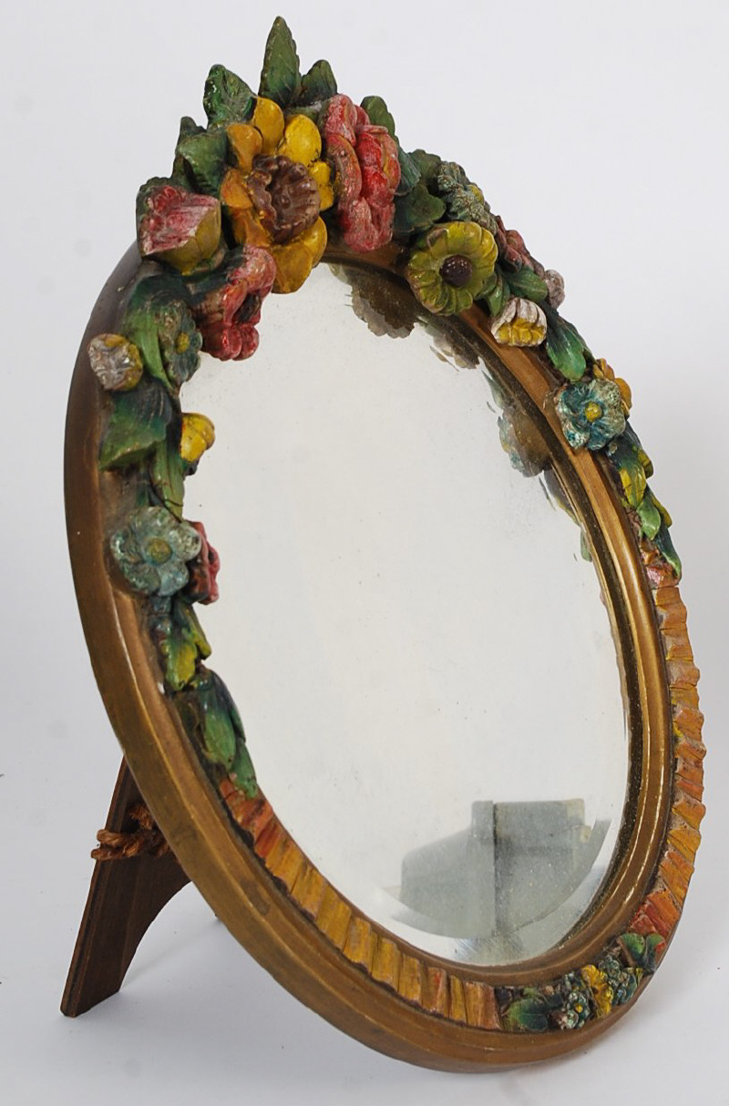 A decorative circular barbola mirror being embellished to the top with flowers over the bevelled