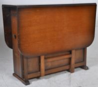A 1930's golden oak drop leaf harvest table having end cupboards to the uprights, drop leaves either