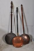 Three Victorian copper bed warming pans with long wooden handles.