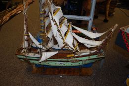 A carved wooden model of a galleon sailing ship with stringed sails and lifeboats.