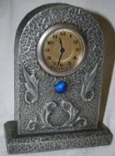 An Arts & Crafts liberty style pewter arched case clock with embossed foliate decoration and blue