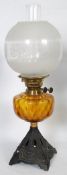 A Victorian cast iron and amber glass oil lamp. The ebonised cast iron base with a decorative