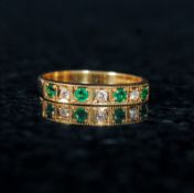 An 18ct gold emerald and diamond half eternity ring. The channel set emeralds interspersed with