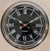 A large polished metal wall clock in the station style having ebonised facia and quartz battery