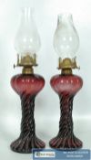 A pair of oil lamps, with Cranberry glass basses in a mottled red and black colouring design. 43cm