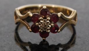 A 9ct gold hallmarked ladies flower ring having diamond chip surround with rubys fret pierced