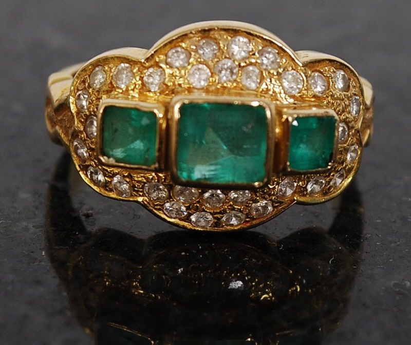 An 18ct gold ladies solitaire ring. The 3 central set emerald stones surround by pave set