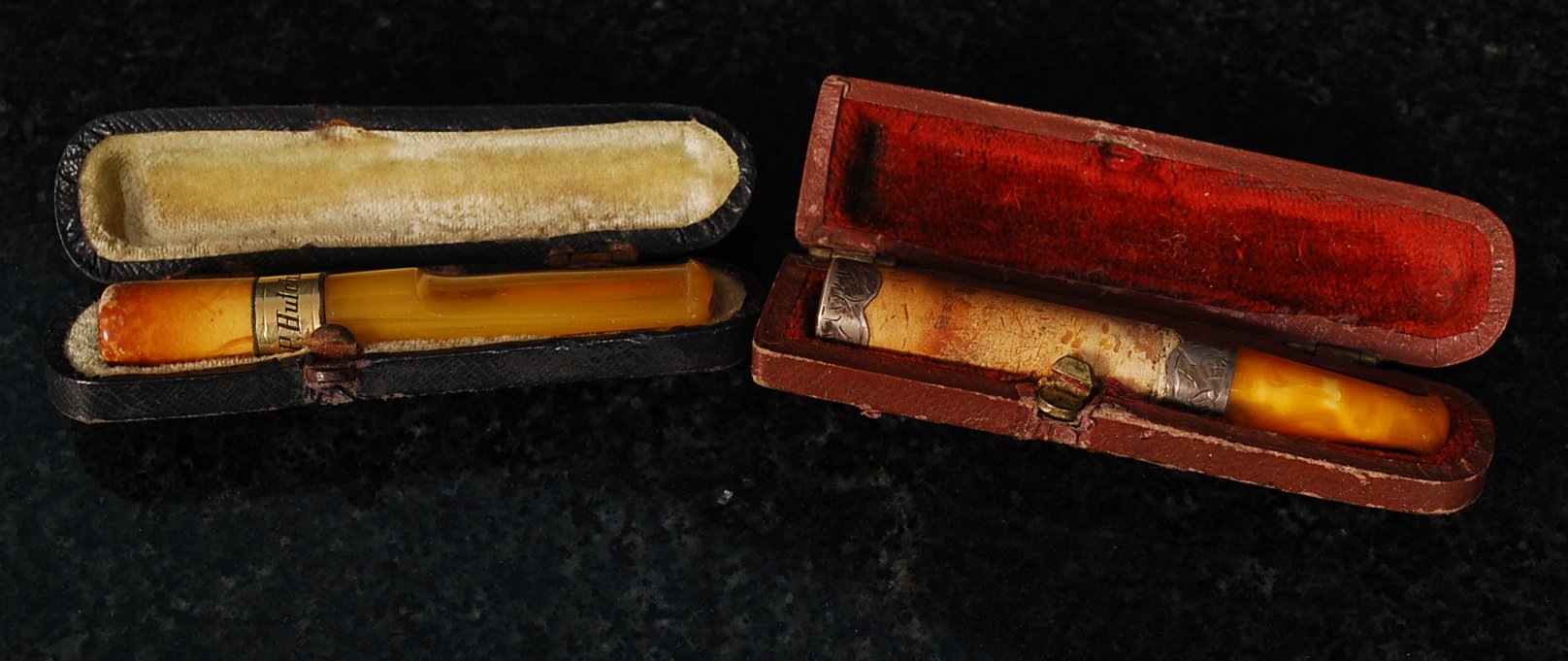 2 silver cigarette holders. 1 being amber and yellow metal, the other amber and white metal.