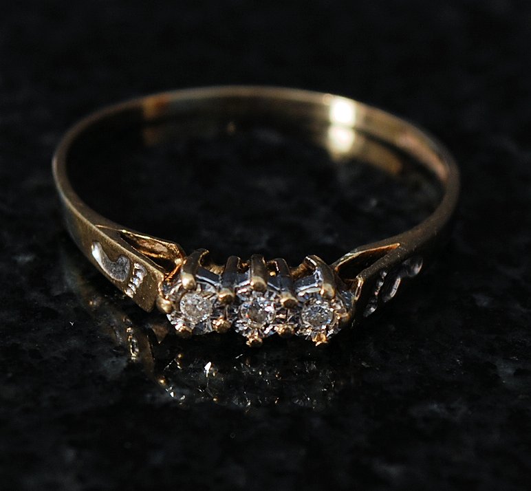 A 9ct gold 3 stone diamond ring. The 3 stones set on bevel mounts with the hoop chase engraved