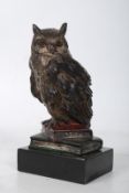 A bronze figurine of an owl standing on books.