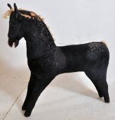A 1950's straw filled rocking horse having part wooden face with black fabric upholstery (minus