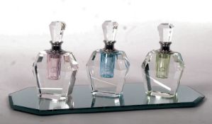 A set of three Art Deco style glass perfume bottles, on a bevelled glass stand (23cm long)