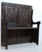 An 18th century Jacobean revival solid carved oak hall settle. The panelled central seat being