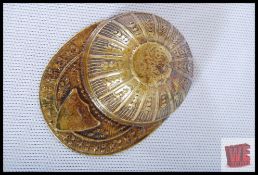 A brass match striker / vesta in the form of a cap with shield decoration. 6cm long.