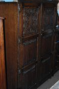 A 1930's Jacobean Revival oak double wardrobe having carved pictorial and linen fold panel doors