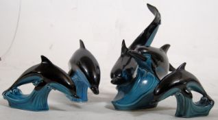 Four Poole Pottery statues depicting black dolphins on mottled green bases. Marked 'Poole' to