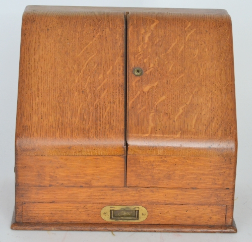 An early 20th Century oak stationery cabinet, the sloping hinged doors enclosing a stepped fitted