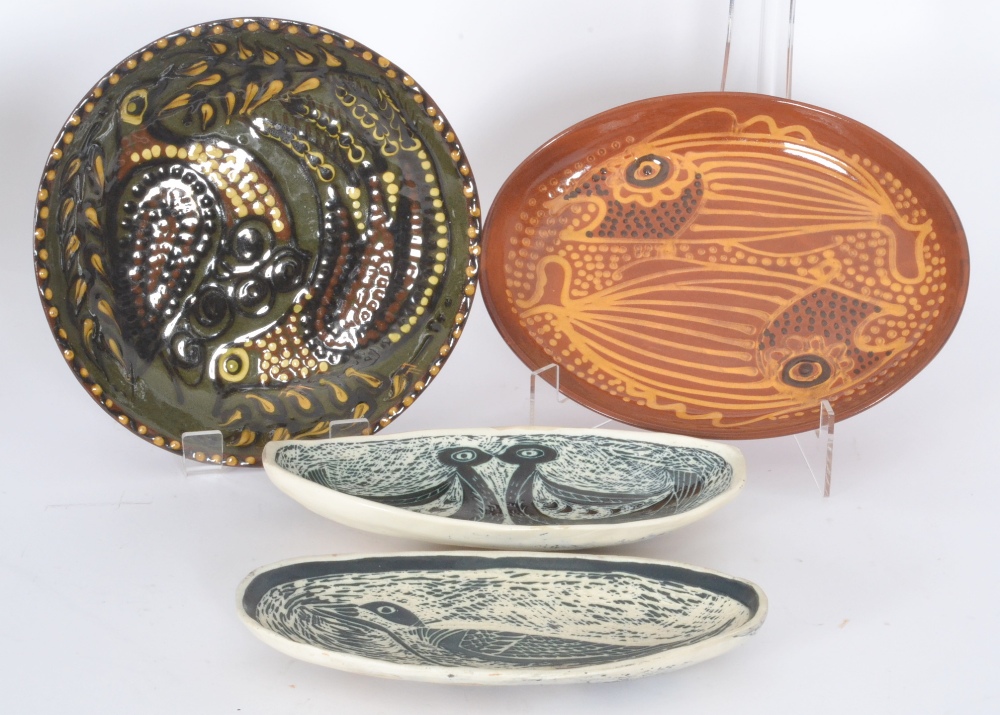 Four 20th Century studio pottery dishes, the first of oval form and decorated with slip trail fish
