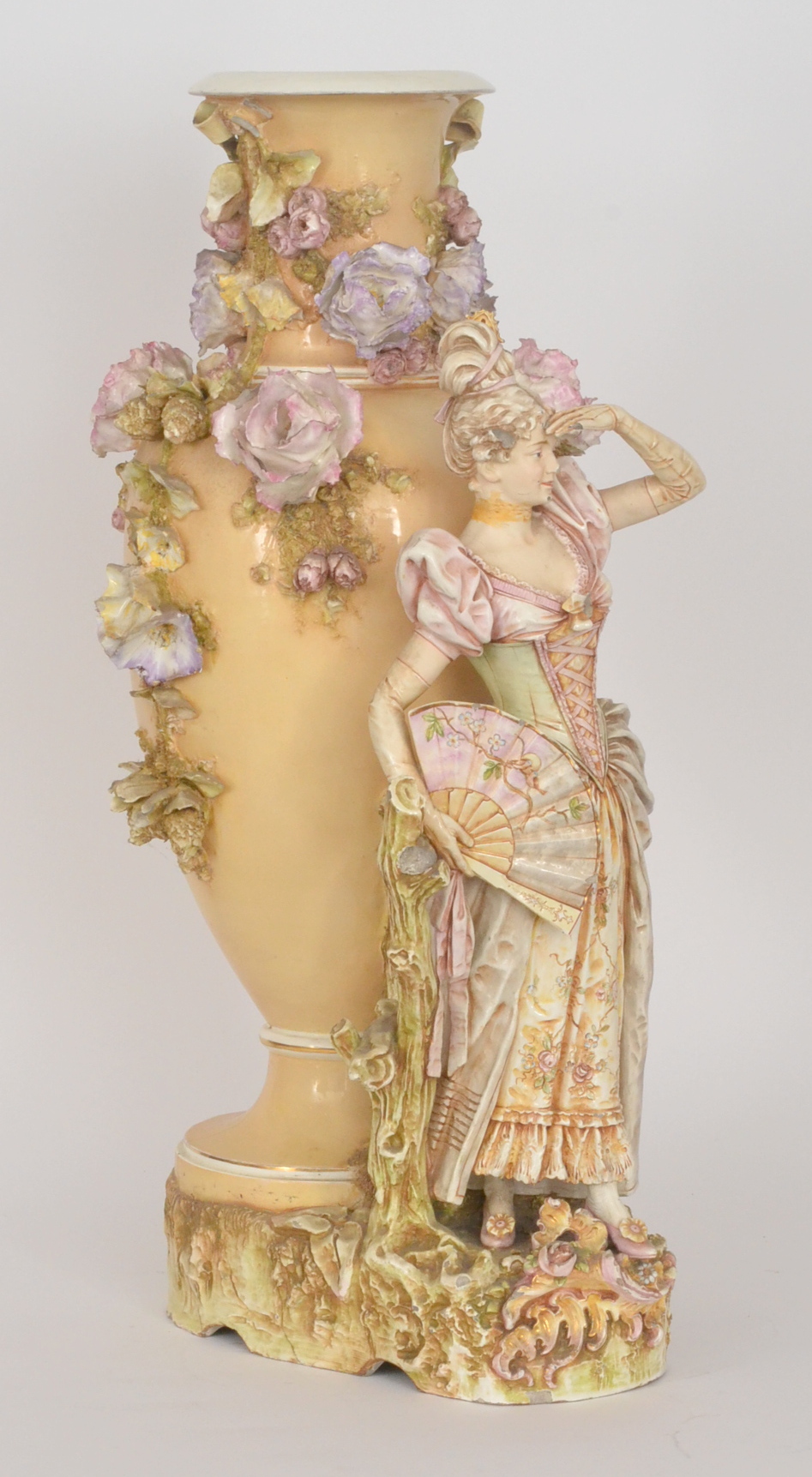 A large late 19th Continental figure of a girl holding a fan resting on a stump with large floral