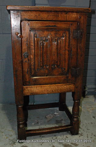 A 20th Century reproduction oak pot cupboard with a linen fold door panel over a turned stretcher
