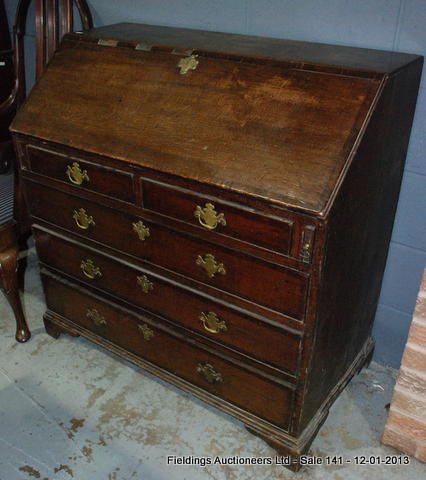 A Georgian oak fall-front bureau enclosing a fitted interior above two short and three long cock-