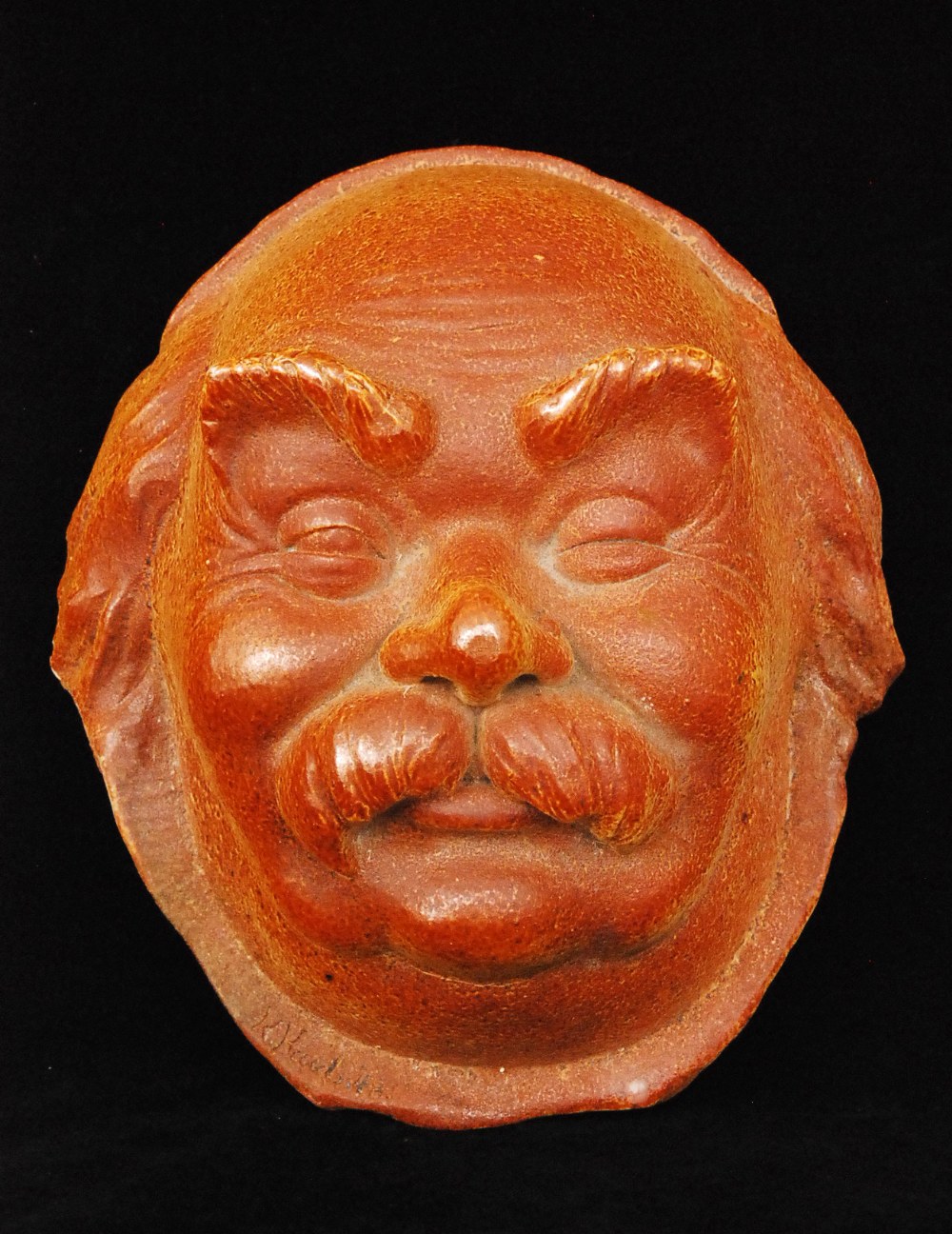 A 20th Century stoneware face mask modelled as a smiling portly gentleman with bushy eyebrows and