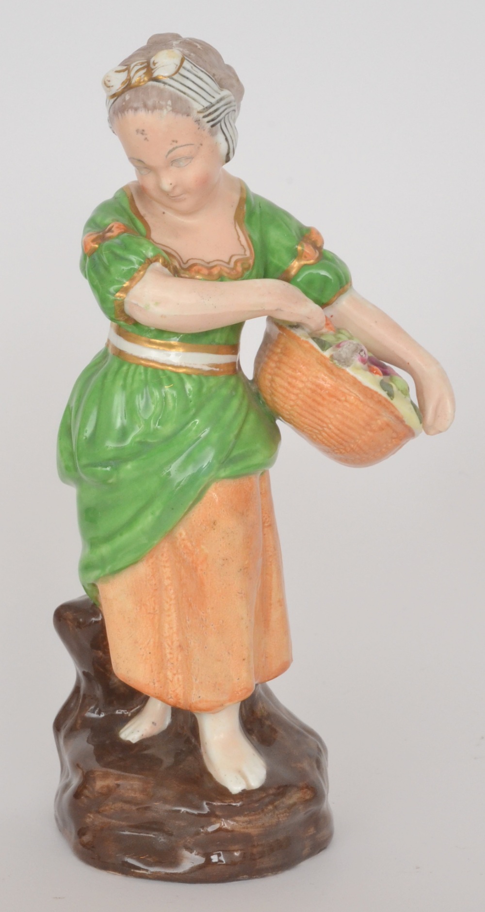 A late 19th Century Continental figure of a lady dressed in green holding a basket of fruit,