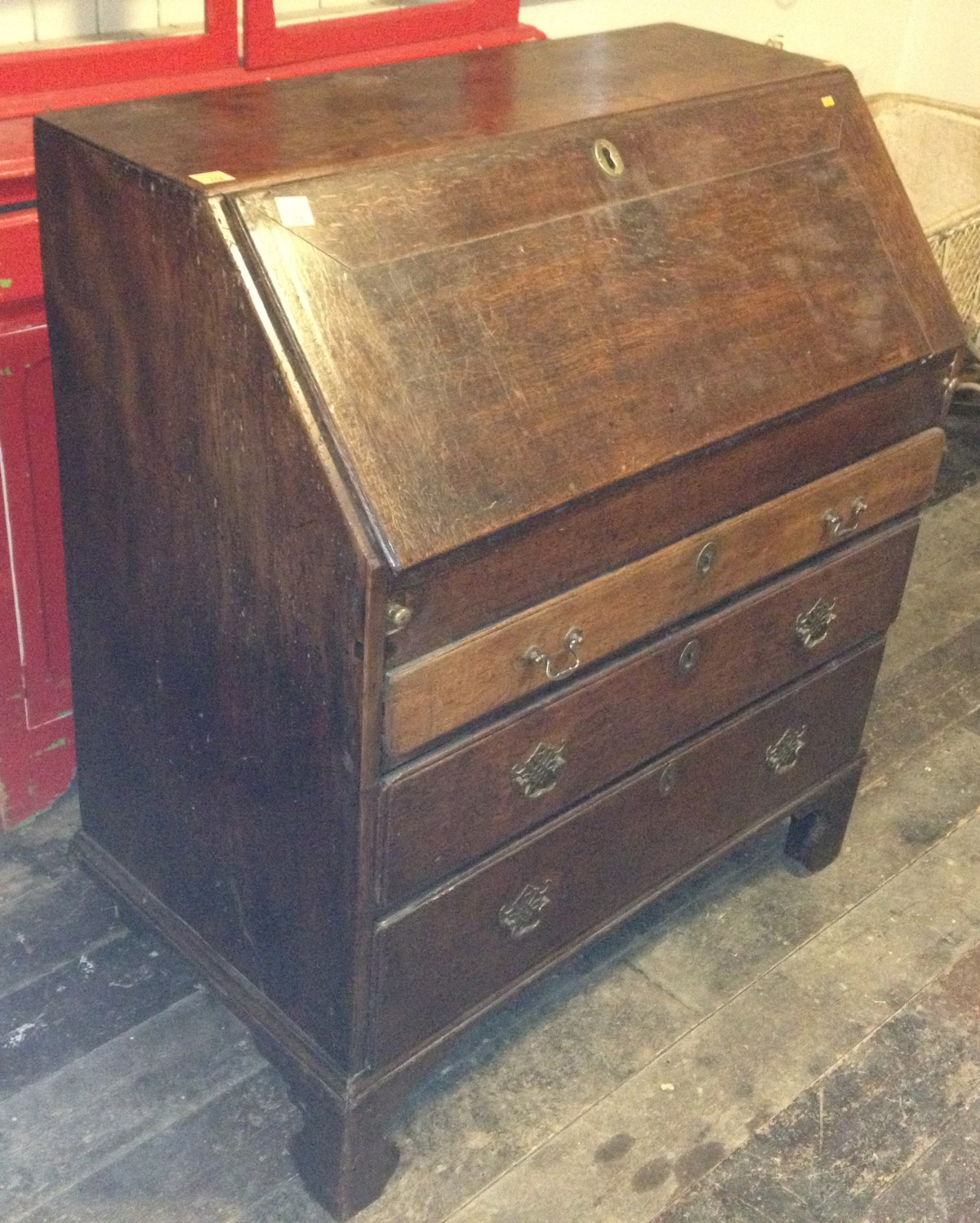 An antique oak drop front Bureau, the interior fitted with a concealed well, over three long drawers