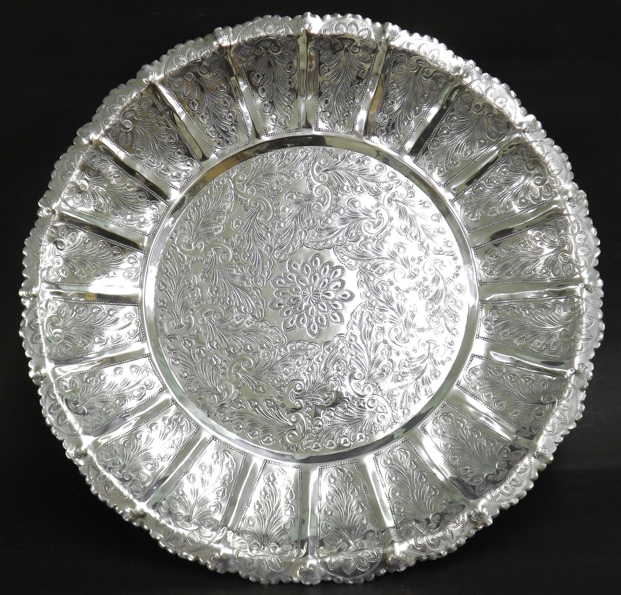 Eastern white metal charger, engraved with scrolled floral decoration upon three shaped feet, 17"