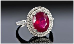 A 14ct White Gold Set Ruby And Diamond Cluster Ring. The oval cut ruby of good quality and colour,