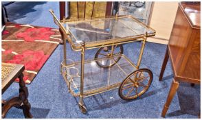 Brass Two Tier Trolley With Glass Shelves. With two large brass spoked wheel and two small wheels,