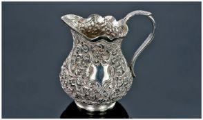 An Indian Silver Kutch Cream Jug, baluster shape with scroll handle and profuse raised floral