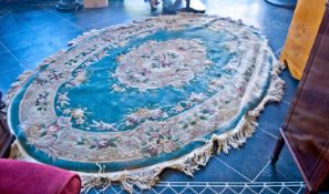 Large Chinese Woolen Rug, oval, with floral patterning on a blue ground, white tasselled edges.