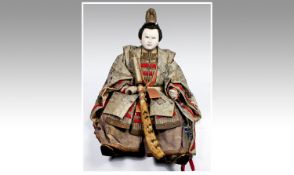 Japanese Seated Samurai Doll Figure with a lacquered face, garbed in fine clothing and holding a