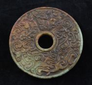A Chinese brown and green jadeite archaistic bi disc, carved in low relief with taotie masks and