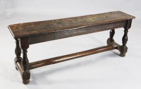 An early 18th century oak bench, the baluster supports united by a rounded stretcher, W.4ft 8in.