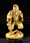 A Japanese stained ivory figure of a farmer, Taisho period, wearing robes holding a hoe with a