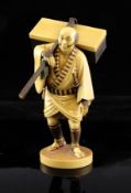A fine Japanese ivory stained okimono of a travelling man, Taisho period, carrying a case upon his