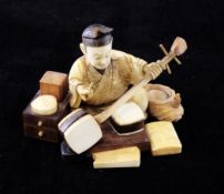 A Japanese ivory and wood figure of a musical instrument maker, early 20th century, flanked by boxes