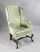 An early 18th century wingback armchair, with scrolling arms, walnut cabriole legs and turned