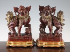 A pair of Chinese red lacquered and gilt decorated wood figures of Buddhist lions, one resting its