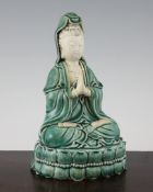 A Chinese green glazed part biscuit Dehua seated figure of Guanyin, holding her hands in prayer,