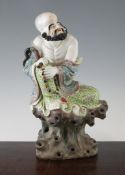 A Chinese famille rose enamelled figure of a seated Luohan, holding a rosary, upon a rock work base,