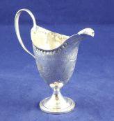 A George III silver helmet shaped pedestal cream jug, with engraved foliate decoration and armorial,