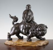 A Japanese bronze figure of a deity riding a Buddhist lion, Meiji period, holding a scroll in his