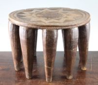 A circular carved hardwood nupe stool, with ten tapering legs and cross hatched decoration, 14in.