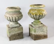 A pair of yellow stone Carnkirk garden urns, with half gadrooned bodies, on pedestal bases, W.1ft