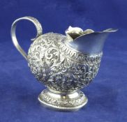 A late 19th century Indian silver cream jug, of askos form, embossed with scrolling foliage,